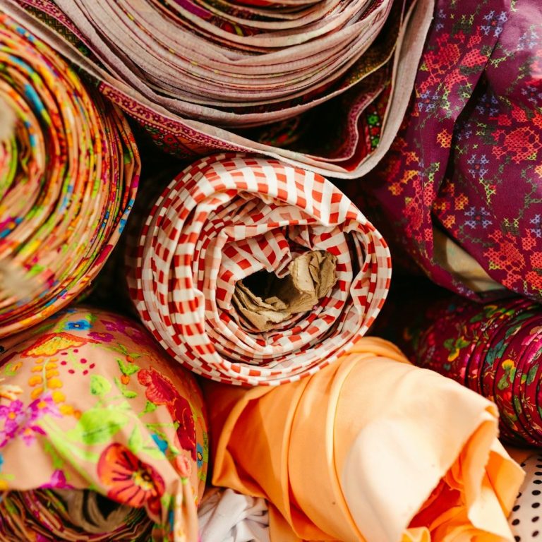 Colourful rolls of patterned fabric in various textures and designs.